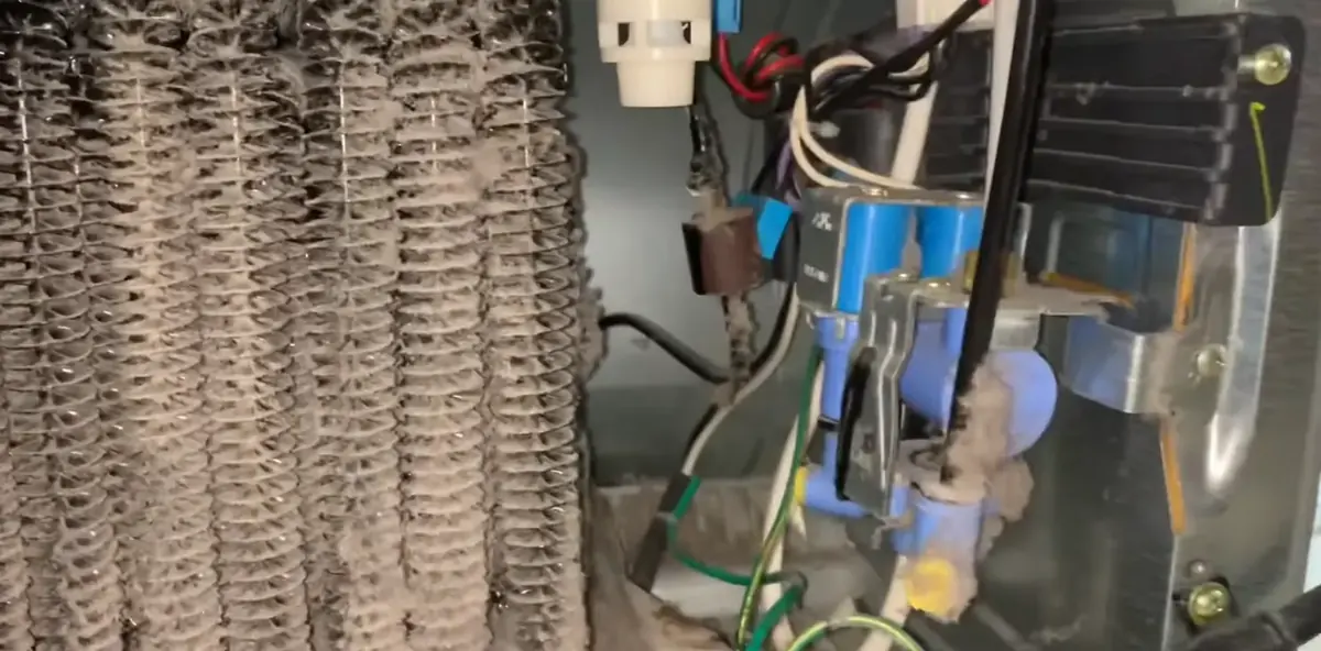 Dusty condenser coils and water inlet valve behind a Bradenton refrigerator